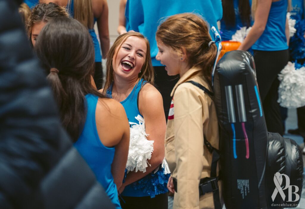 A child wearing a costume standing in front of a member of DanceBlue surrounded by people in the 2022 Halloween party.